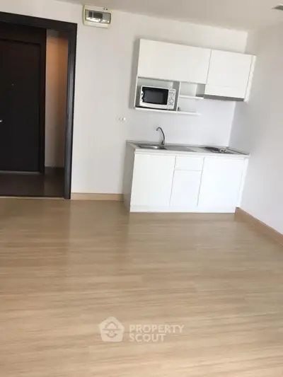 Modern minimalist kitchen with microwave and sleek cabinetry in open layout apartment.
