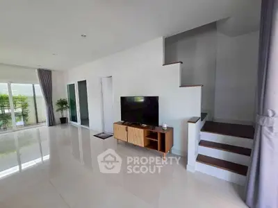 Spacious modern living room with sleek staircase and large windows offering natural light.