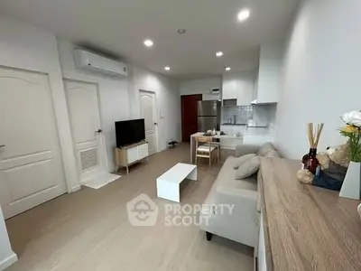 Modern open-layout living room with kitchen, featuring sleek furniture and bright lighting.