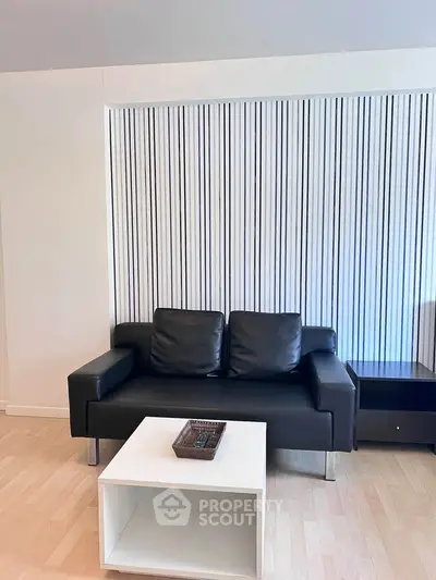 Modern living room with sleek black sofa and stylish white coffee table on light wood flooring.