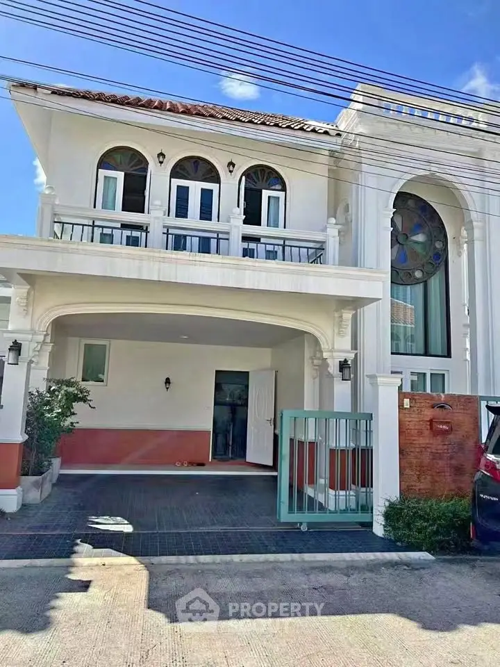Elegant two-story house with arched windows and spacious driveway in sunny neighborhood.