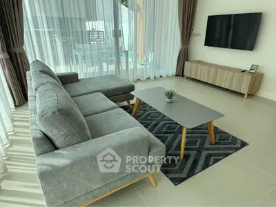 Modern living room with stylish gray sofa, sleek coffee table, and wall-mounted TV, flooded with natural light.