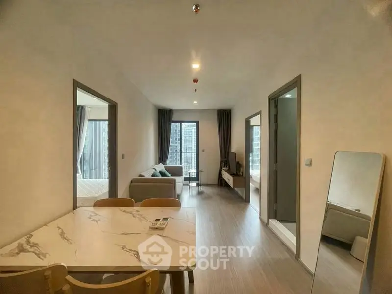 Modern apartment interior with open living and dining area, featuring sleek furniture and large windows.