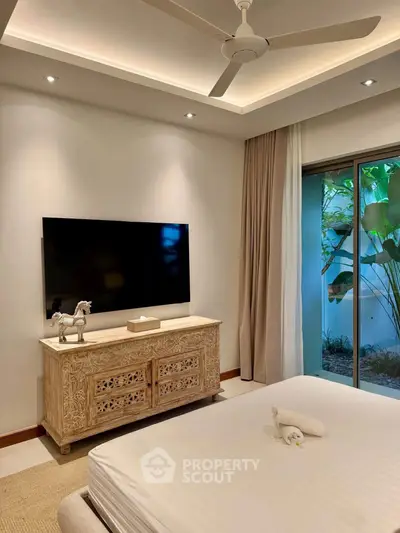 Luxurious bedroom with elegant decor and garden view, featuring a mounted TV and stylish ceiling fan.