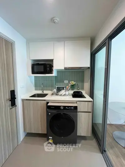 Modern compact kitchen with washer and microwave, sleek cabinetry, and glass door leading to balcony.
