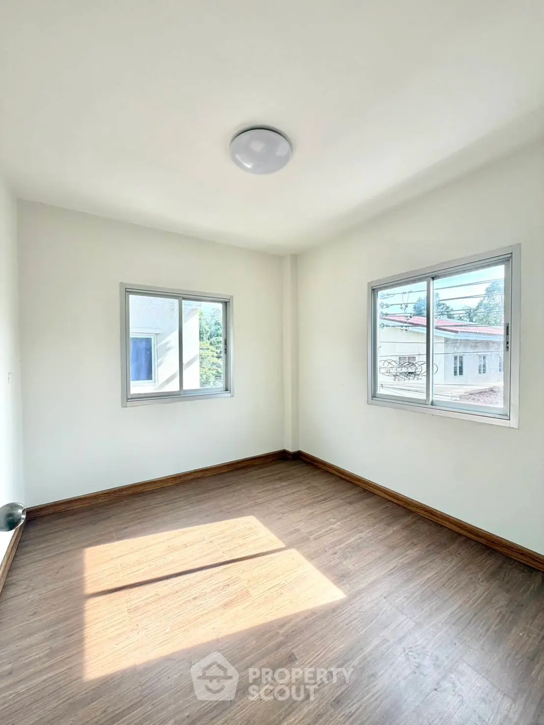 Bright empty room with wooden flooring and large windows offering natural light and views.