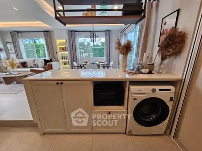Stylish open-plan living room with modern kitchen and laundry area, featuring elegant decor and natural light.