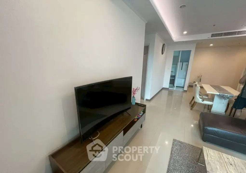 Modern living room with sleek TV unit and dining area in open layout apartment.
