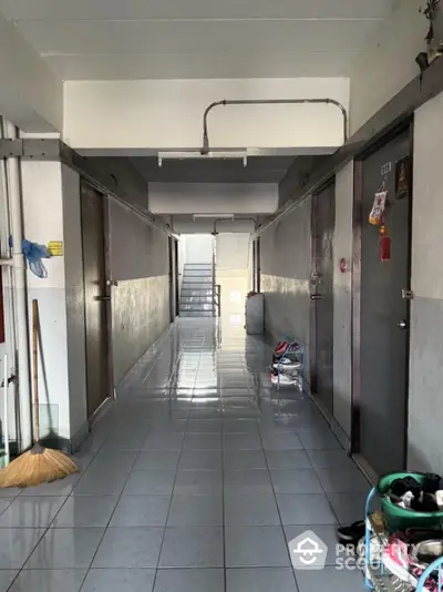 Apartment corridor with tiled floor and utility items, showcasing a typical residential hallway.