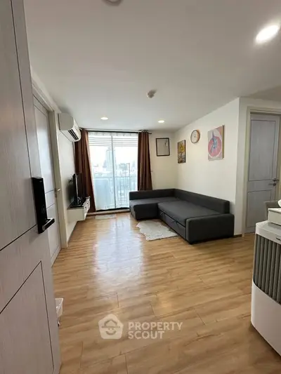 Modern living room with wooden flooring, large window, and stylish gray sofa in a high-rise apartment.