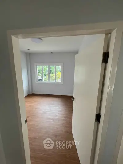 Spacious empty room with wooden flooring and large window offering natural light.