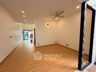 Spacious modern living room with wooden flooring and ceiling fan, leading to open kitchen area.