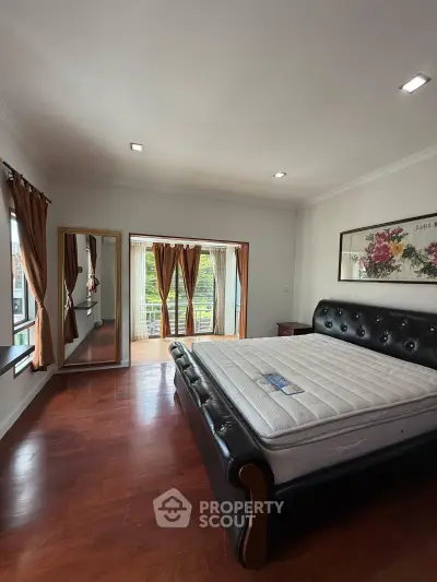 Spacious bedroom with elegant hardwood floors and large windows offering natural light and garden views.