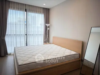 Spacious bedroom with large window and modern furnishings in a stylish apartment.
