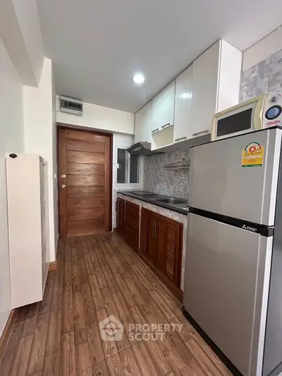Modern kitchen with wooden cabinets, stainless steel fridge, and sleek countertops in a cozy apartment.