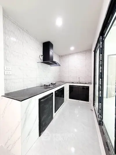 Modern kitchen with sleek black countertops and gas stove in a bright, minimalist design.
