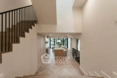 Elegant open-plan kitchen with modern design and natural light, featuring sleek cabinetry and stylish staircase.