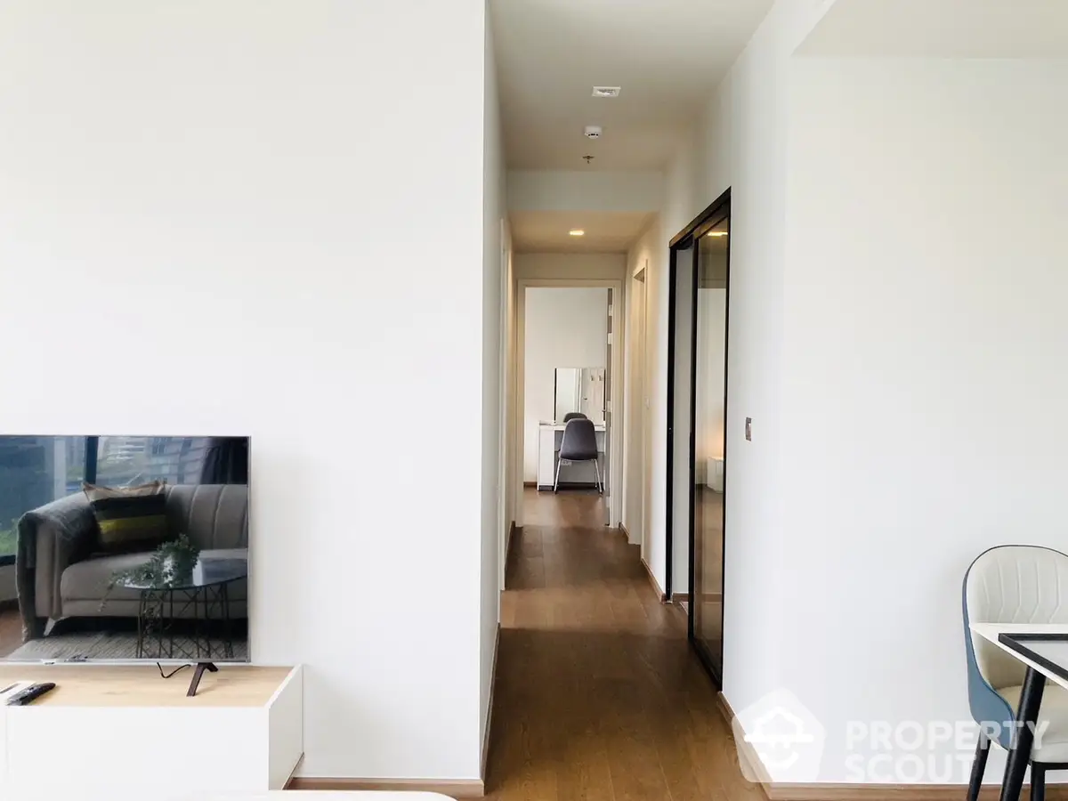 Bright and airy modern apartment interior with a spacious open-plan living area leading to a cozy hallway, featuring sleek furnishings and wood flooring.