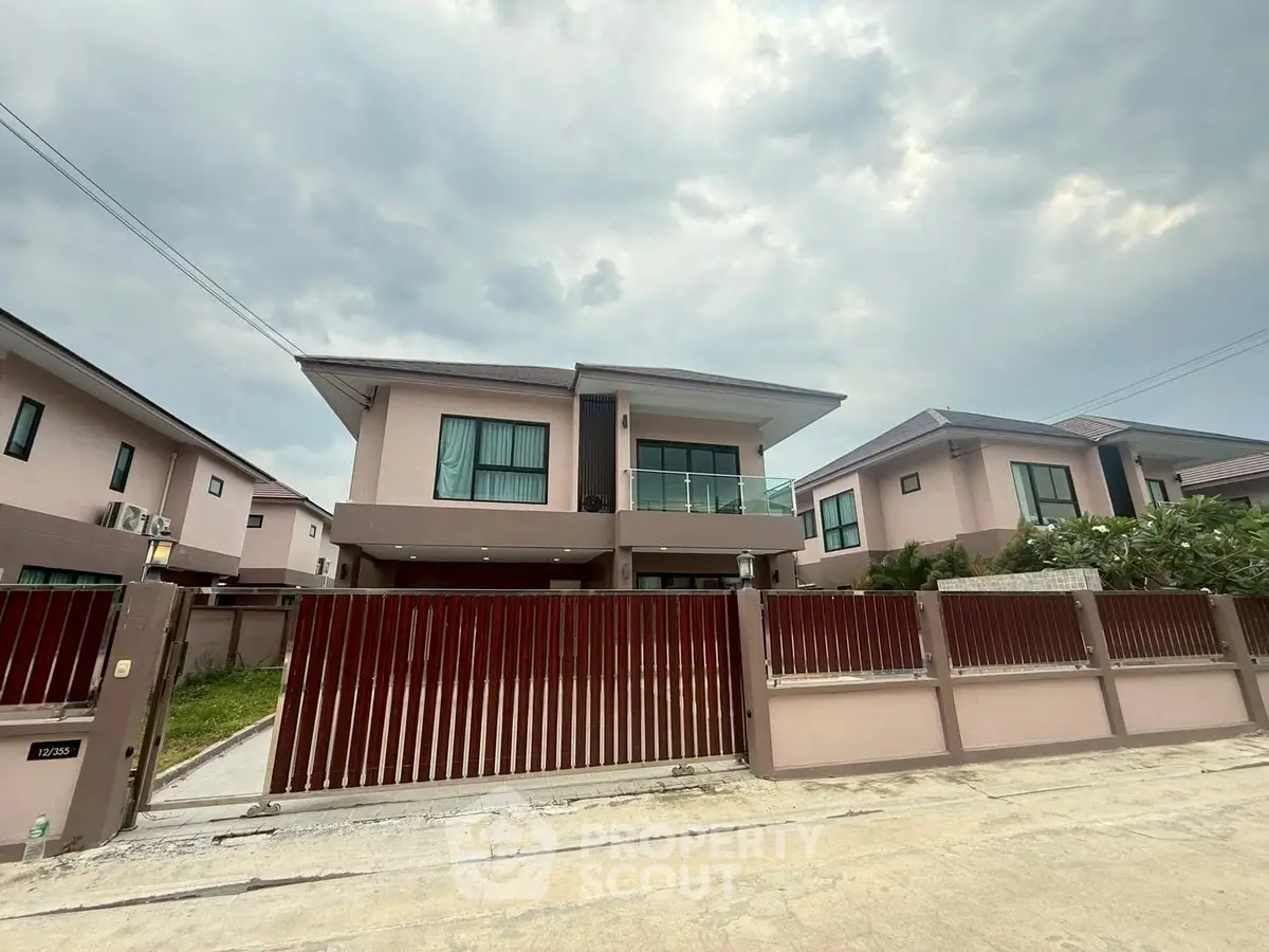 Modern two-story house with gated entrance and cloudy sky backdrop.