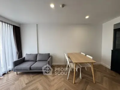 Modern living room with stylish gray sofa and wooden dining table, featuring elegant herringbone flooring.