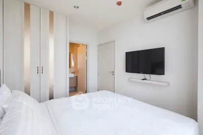 Modern bedroom with wall-mounted TV and ensuite bathroom in stylish apartment.