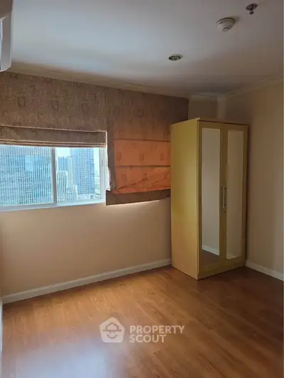 Spacious bedroom with wooden flooring and city view, featuring a large wardrobe and ample natural light.