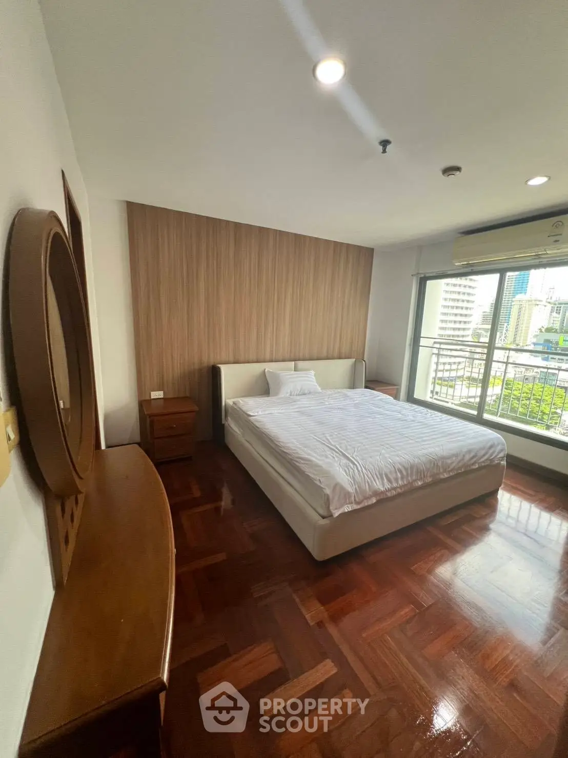Spacious bedroom with wooden flooring and city view balcony in modern apartment