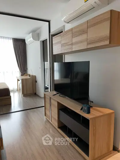 Modern living room with sleek wooden furniture and large TV, featuring a cozy bedroom view.