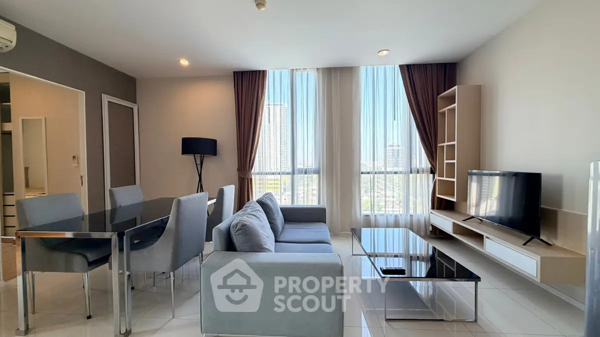 Modern living room with sleek furniture and large windows offering city views.