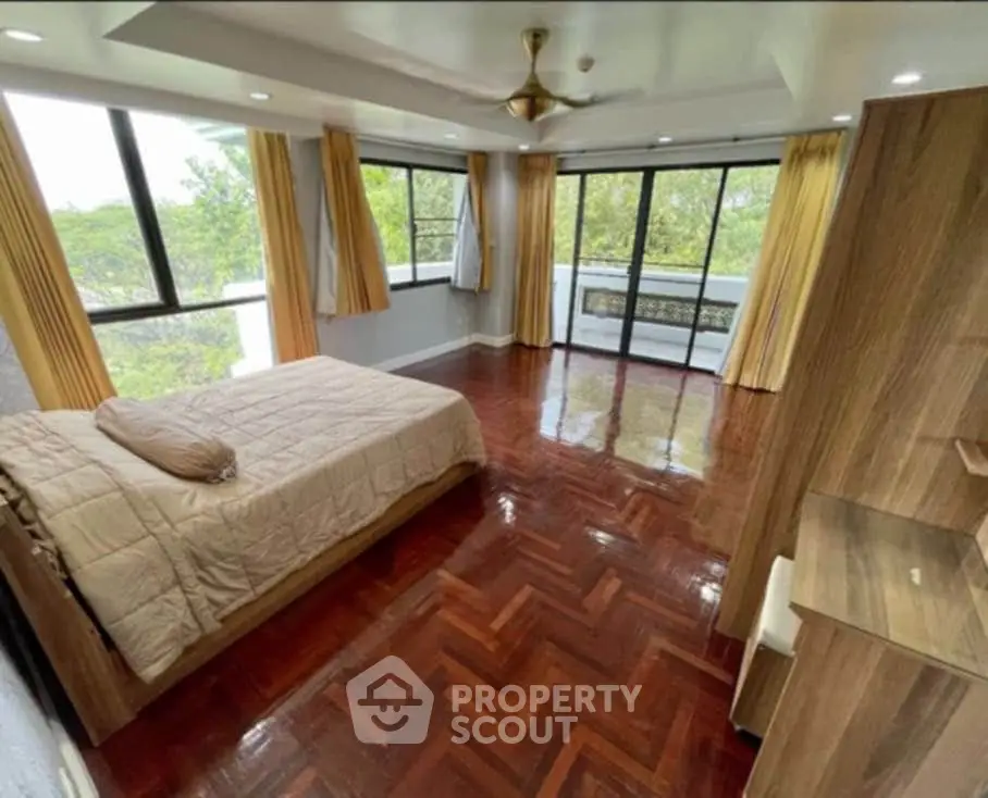 Spacious bedroom with large windows and wooden flooring offering serene views