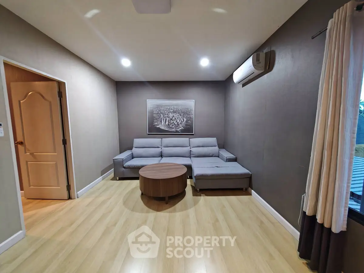Modern living room with sleek grey sofa and wooden flooring, featuring elegant lighting and air conditioning.