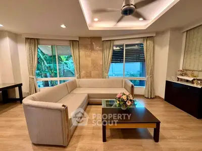 Elegant living room with modern sofa, glass coffee table, and large windows offering garden view.