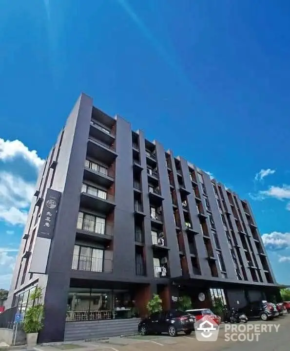 Modern apartment building with clear blue sky and parking area in front.