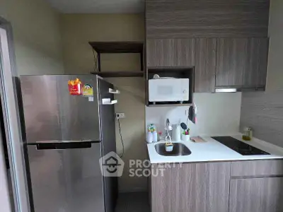 Modern kitchen with sleek cabinetry, stainless steel fridge, and built-in microwave in a compact layout.