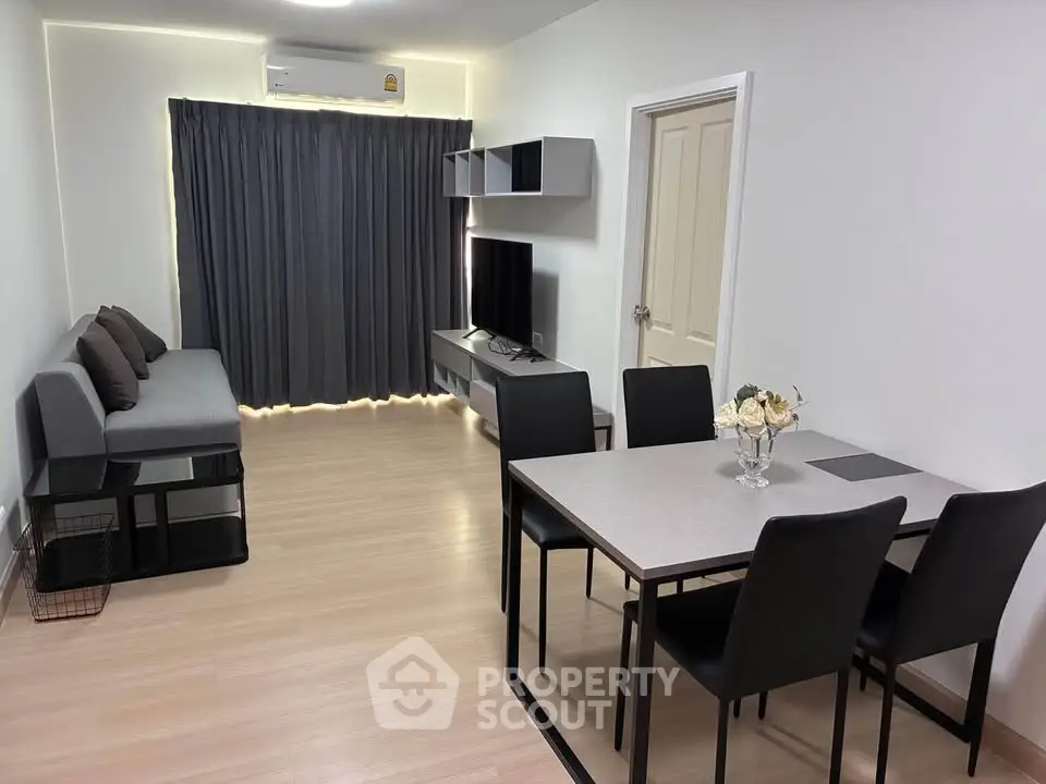 Modern living room with sleek furniture and dining area, featuring a cozy sofa and flat-screen TV.