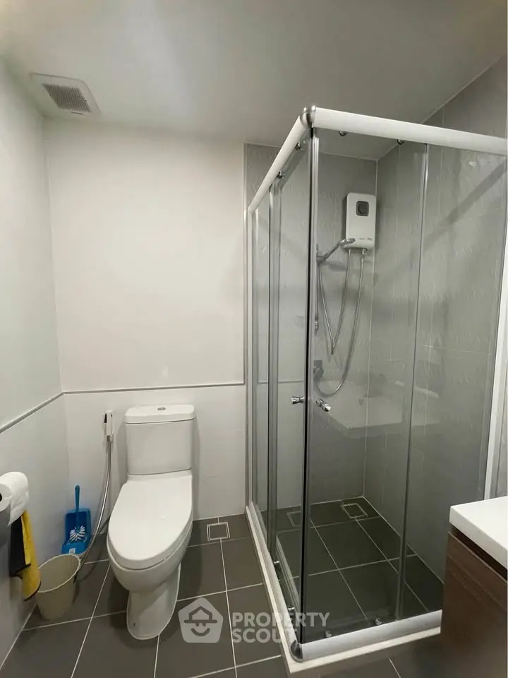 Modern bathroom with glass shower enclosure and sleek tile flooring.