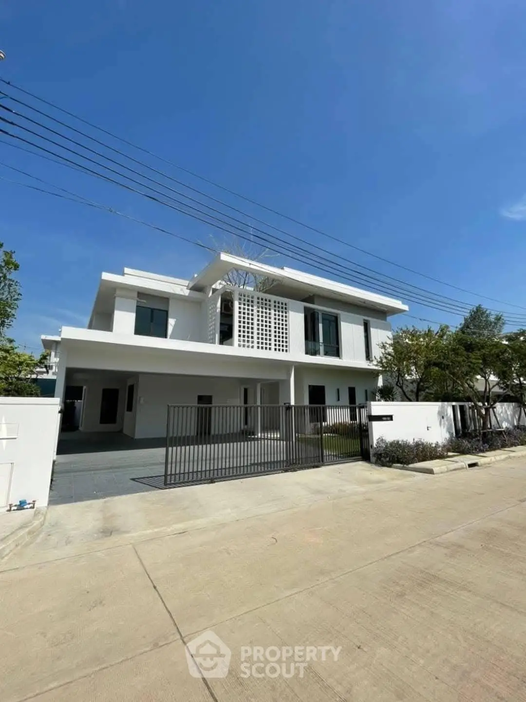 Stunning modern white villa with spacious driveway and lush greenery under clear blue sky.