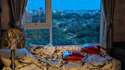 Cozy bedroom with stunning city view through large window, featuring elegant decor and plush bedding.