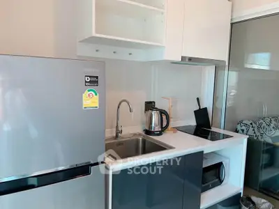 Modern kitchen with sleek appliances and compact design, featuring a fridge, sink, and electric stove.
