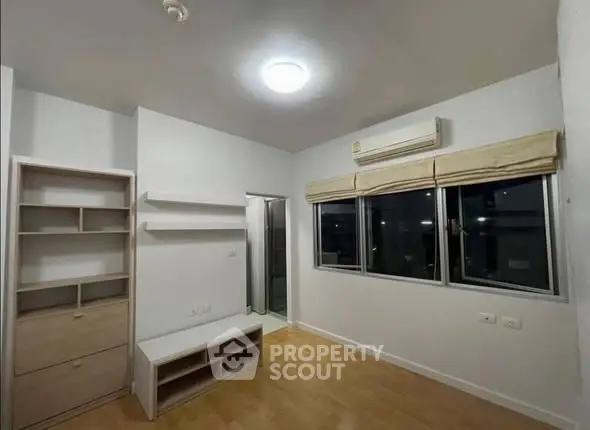 Modern bedroom with wooden flooring and large window, featuring built-in shelves and air conditioning.