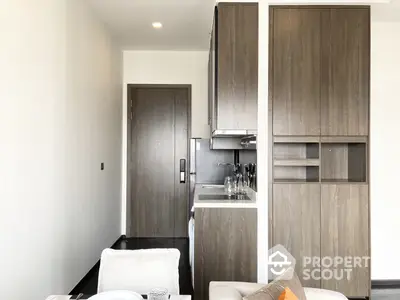 Modern compact kitchen with sleek wooden cabinetry and integrated appliances, adjacent to a cozy living area, perfect for urban living.