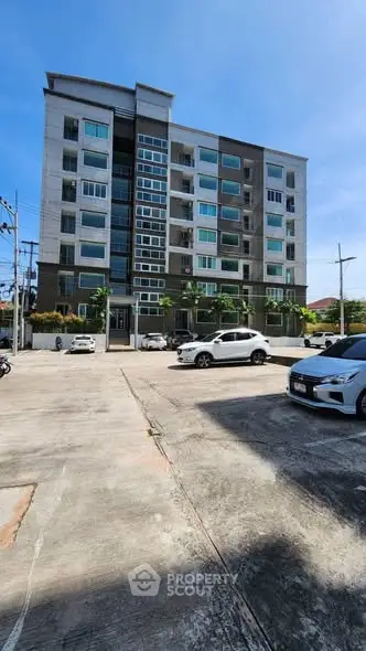 Modern apartment building with spacious parking area and clear blue sky.