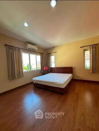 Spacious bedroom with wooden flooring and natural light from large windows.