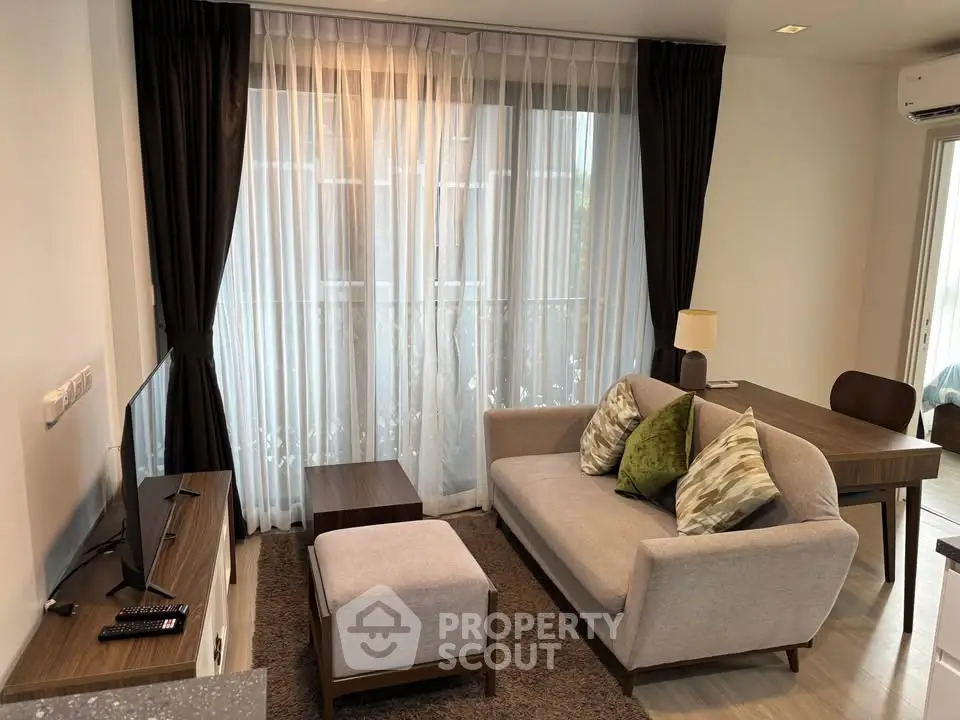 Cozy living room with modern furniture and large window draped with elegant curtains.