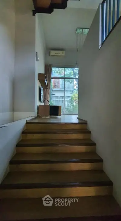 Modern interior with wooden staircase leading to a bright living area with large windows.