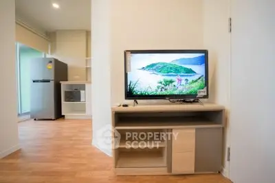 Modern living room with wooden flooring, TV, and open kitchen layout featuring fridge and microwave.