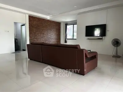 Spacious modern living room with brown leather sofa and exposed brick wall, perfect for relaxation.