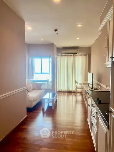 Spacious living room with wooden flooring and natural light, featuring a cozy sofa and modern decor.