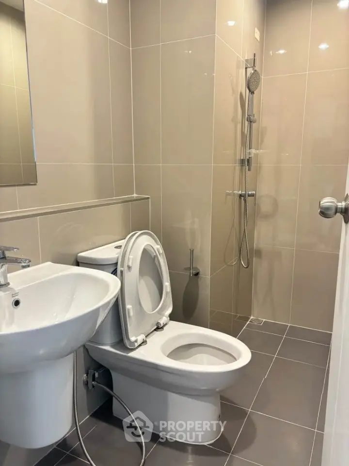 Modern bathroom with sleek fixtures and neutral tiles, featuring a shower and toilet.