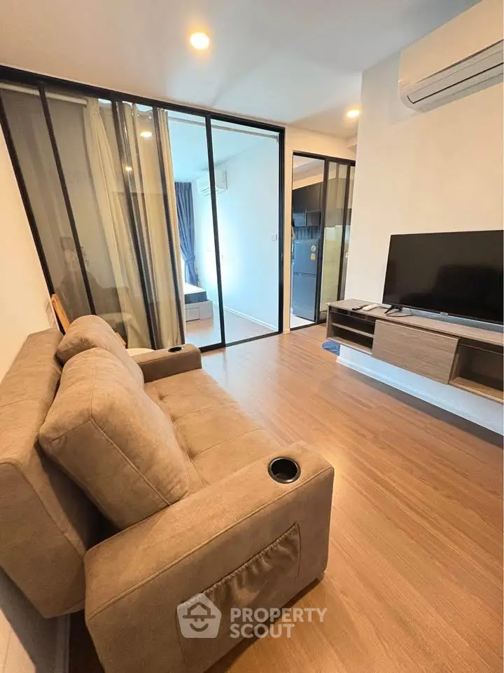 Modern living room with cozy sofa, TV, and sliding glass doors leading to bedroom.